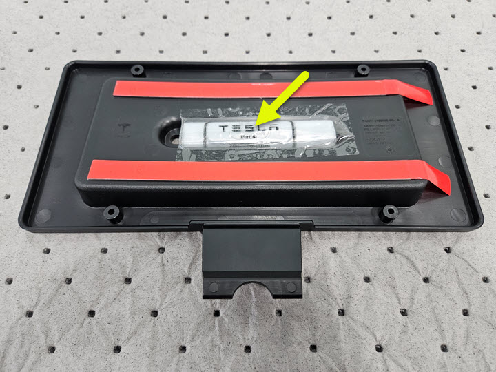 前车牌架的照片，箭头指向固定在内侧的紧固件的包装